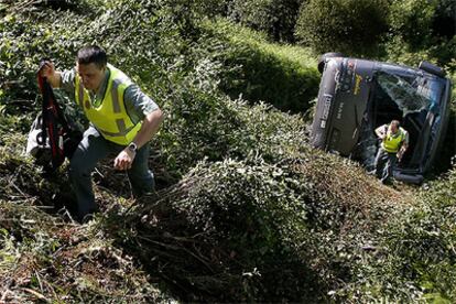 Dos guardias civiles inspeccionan el lugar donde cayó el autocar, que aparece volcado.