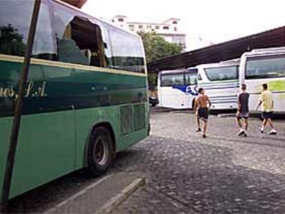 Tres jóvenes viajeros pasan junto a un autobús con la luna rota por los piquetes, que obligaron al conductor a volver ayer a Sevilla.