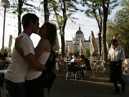 Dos j&oacute;venes se besan en una terraza entre el Paseo del Prado y la plaza de Oriente, detr&aacute;s la Catedral de la Almudena de Madrid 