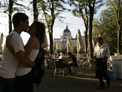 Dos jóvenes se besan en una terraza entre el Paseo del Prado y la plaza de Oriente, detrás la Catedral de la Almudena de Madrid