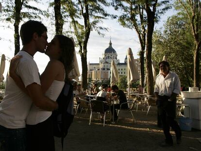 Dos j&oacute;venes se besan en una terraza entre el Paseo del Prado y la plaza de Oriente, detr&aacute;s la Catedral de la Almudena de Madrid 