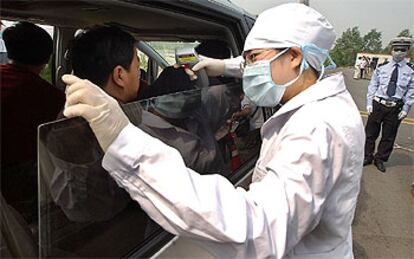 Un médico toma la temperatura a los pasajeros que salen del aeropuerto de Pekín.