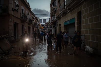 Vecinos y voluntarios caminan al anochecer por una de las calles inundadas por el lodo que dej a su paso la riada que tuvo lugar el pasado martes, en Paiporta, viernes 1 de noviembre de 2024.