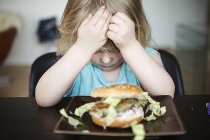 Una niña no quiere comer una hamburguesa.