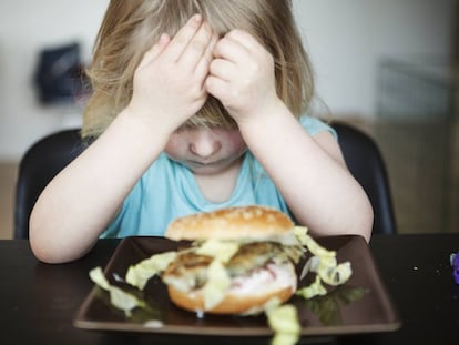 Una niña no quiere comer una hamburguesa.