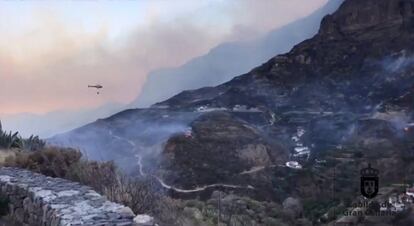 Houses dot the hillside as a helicopter flies to drop water over wildfires at Artenara, Gran Canaria.