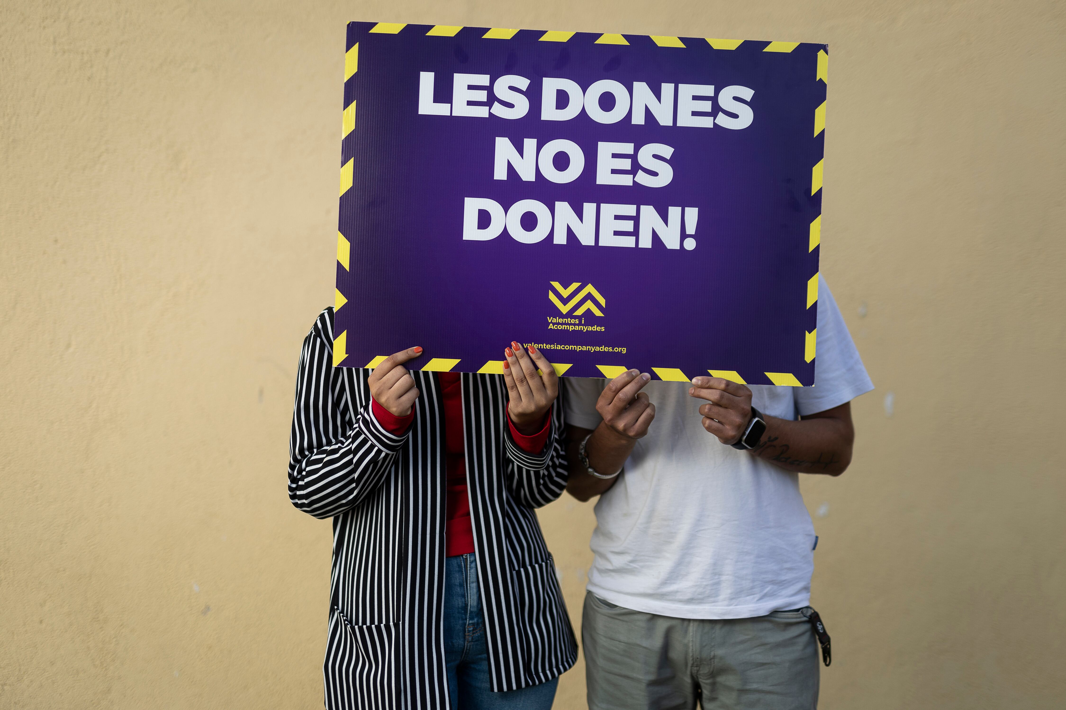 Sara y Arush, con un cartel de la entidad Valentes i Acompanyades en el que se lee, en catalán, 