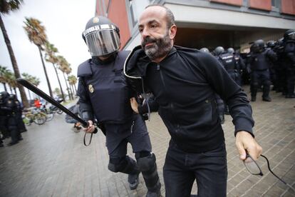 Un  antidisturbio (UIP) de la Policía Nacional acompaña a un ciudadano a salir del perímetro de seguridad en la Escola Mediterránea de la Barceloneta en Barcelona. Incidentes entre votantes y Guardia Civil y Policía Nacional en el día del referéndum ilegal independentista catalán del 1-O. Desafío independentista en Cataluña. 
