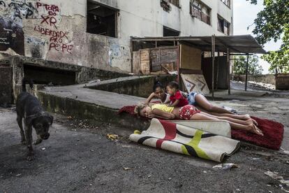 Dos jóvenes juegan con un bebé sobre una alfombra delante del edificio abandonado del IBGE, en la favela de Mangueira, Río de Janeiro, Brasil.