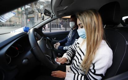 Una alumna de autoescuela junto a su profesor desinfecta el volante del coche para reiniciar las clases.