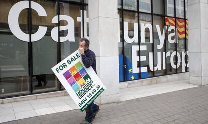 Un hombre con un cartel de se vende pasa por delante de la fachada de la sede de la Embajada de la Generalitat de Cataluña en Bruselas (Bélgica).