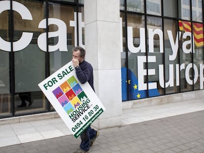 Un hombre con un cartel de se vende pasa por delante de la fachada de la sede de la Embajada de la Generalitat de Cataluña en Bruselas (Bélgica).