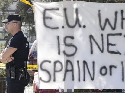 Un agente de la policía en Chipre junto a una pancarta que dice: “¿UE, quién es el próximo? España o Italia”.