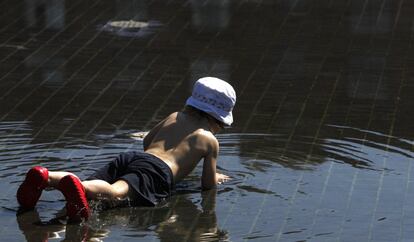 Un niño tumbado en un charco formado por una de las fuentes de Madrid Río, 5 de julio de 2013. Un flujo de aire cálido y seco de origen africano afectará a las Islas Canarias a partir del próximo martes.