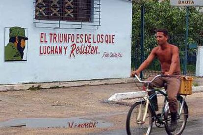 Un cubano pasa en bicicleta junto a un cartel con una consigna y la imagen de Fidel Castro en La Habana.