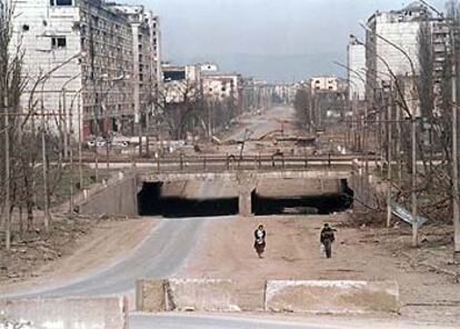 Una pareja de chechenos camina por la calle principal de Grozni, asfaltada a medias, entre edificios destruidos.