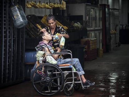 Una madre da de beber agua a su hijo postrado en una silla de ruedas en Caracas.