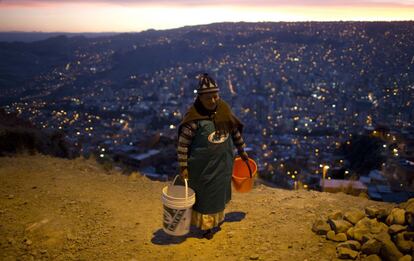 Una mujer camina con dos cubos vacíos para recoger agua, en La Paz (Bolivia).