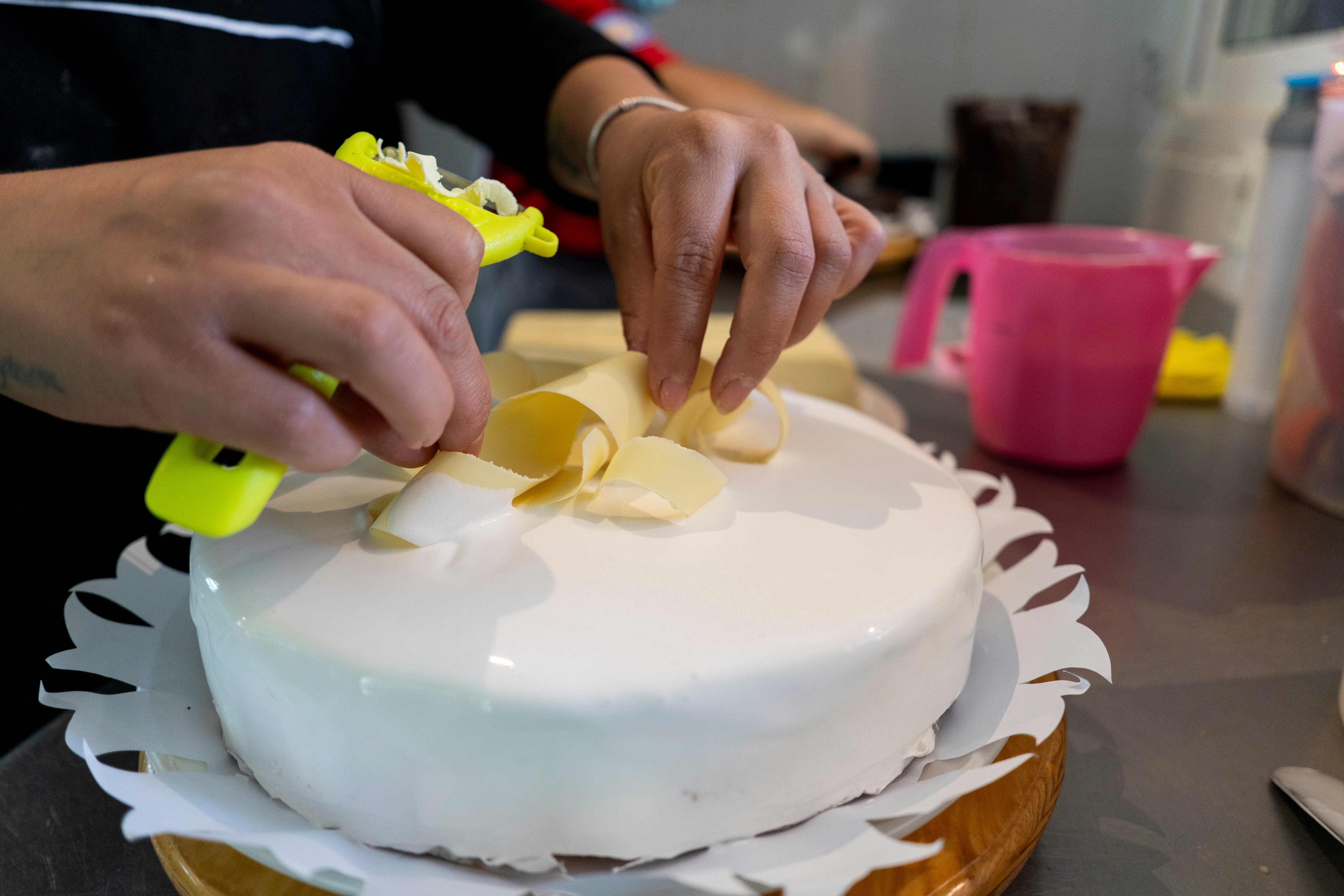 Una repostera decora un pastel de tres leches con rayadura de chocolate blanco.