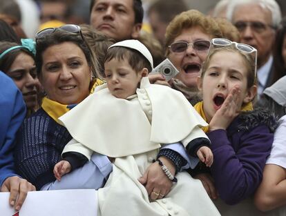 Una madre sostiene a su hijo vestido de Papa, antes de la llegada del papa Francisco, en la plaza de San Pedro en el Vaticano, 9 de abril 2014.