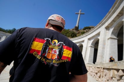 Un hombre con una camiseta que luce la bandera franquista frente al Valle de los Caídos.
