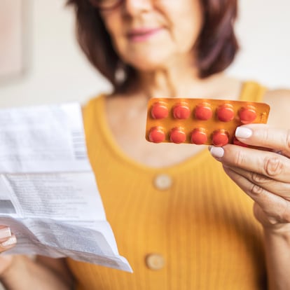 Close up of a Latin woman using medicine pills. She is sitting on bed and reading patient information leaflet.