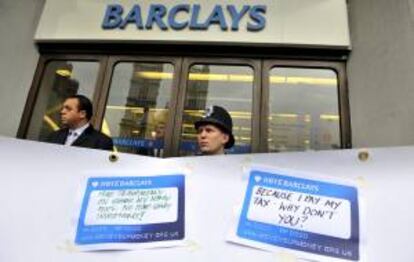 Un policía británico y un guardia de seguridad vigilando tras una pancarta donde los manifestantes pegaban mensajes frente a una sucursal de Barclays, durante una protesta en Londres el pasado miércoles.