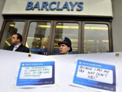 Un policía británico y un guardia de seguridad vigilando tras una pancarta donde los manifestantes pegaban mensajes frente a una sucursal de Barclays, durante una protesta en Londres el pasado miércoles.