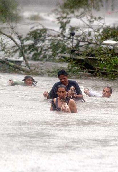 Varias personas intentan cruzan una calle inundada en la ciudad de Lacombe, en Luisiana.