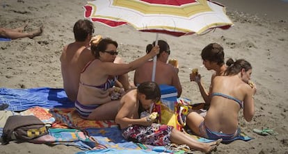 Una familia come sus bocadillos bajo la sombrilla en la arena de una playa de Benalmádena (Málaga).