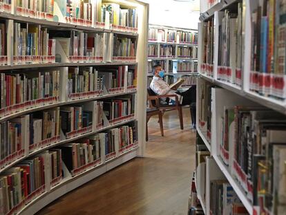 Un lector con mascarilla consulta un libro en una biblioteca de Singapur.