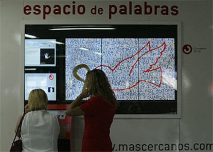 Dos personas, frente a la pantalla del <i>Espacio de palabras,</i> el montaje que sustituirá al <i>santuario</i> de Atocha en homenaje a las víctimas del 11-M.