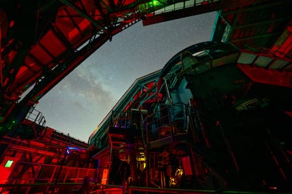 El enorme telescopio del Observatorio Rubin apuntando hacia el cielo nocturno a través de la abertura rectangular de la cúpula.