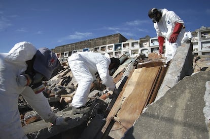 Trabalhadores tentam recuperar um caixão destruído em um cemitério em Penco.