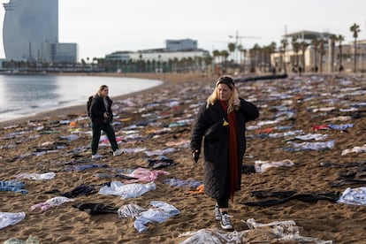 Dos mujeres caminan entre la ropa tendida en la playa de San Sebastián de Barcelona, este lunes. 