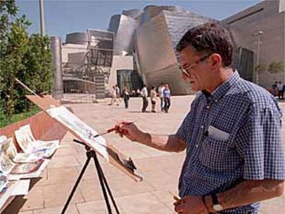 Un artista callejero pintaba ayer cuadros junto al Museo Guggenheim de Bilbao.