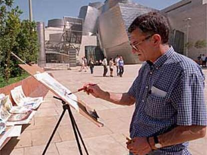 Un artista callejero pintaba ayer cuadros junto al Museo Guggenheim de Bilbao.