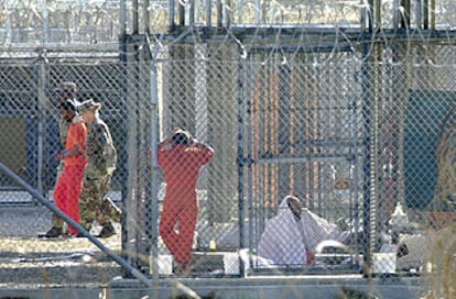 Un preso de Guantánamo es escoltado por dos guardias, mientras otros cautivos permanecen en sus celdas.