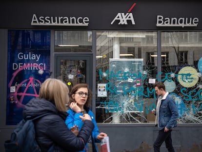 Unos ciudadanos pasan por delante de la sucursal de un banco en París, dañada durante las protestas contra la reforma de las pensiones de Macron, este miércoles.