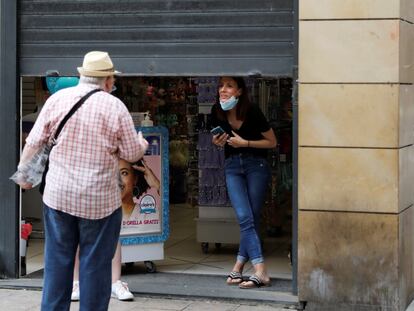 Un comerciante habla con una persona con la persiana medio bajada en Lleida.