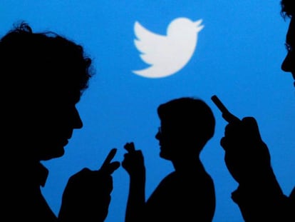 Usuários de celulares em frente ao logotipo do Twitter.