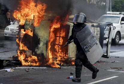 Un integrante de la Policía de Nicaragua pasa frente a un vehículo policial en llamas durante los disturbios por las protestas contra el presidente Ortega en Managua (Nicaragua).