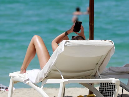 Una mujer consulta su móvil mientras toma el sol en una playa de Mallorca en 2022.