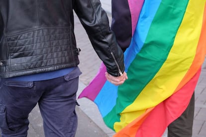 Una pareja se coge la mano con la bandera multicolor. 