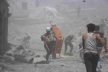 Un trabajador de la Defensa Civil Siria lleva en brazos a un niño herido en una calle de Yisr al-Shugur, tras un ataque aéreo por parte del Gobierno sirio. 