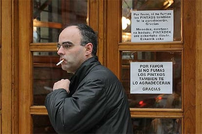 Una persona fuma un cigarrillo ante un bar de San Sebastián que recomienda no hacerño.