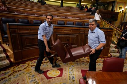 Dos trabajadores de la Cámara baja mueven un asiento en el hemiciclo. 