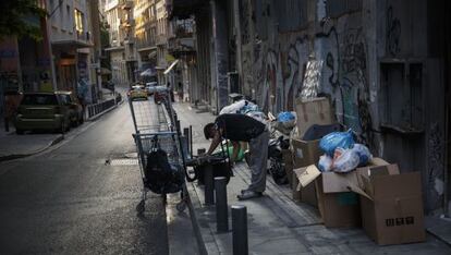 Un hombre recoge trozos de metal de una silla abandonada junto a la basura en Atenas.