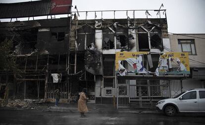 Dos personas caminan el lunes ante edificios quemados durante las protestas, en Teherán.