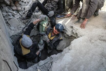 Miembros de Defensa Civil Siria buscan el cuerpo de una víctima bajo las ruinas de un edificio tras un bombardeo después de ser llamados por la propia víctima bajo los escombros, en Duma (Siria).